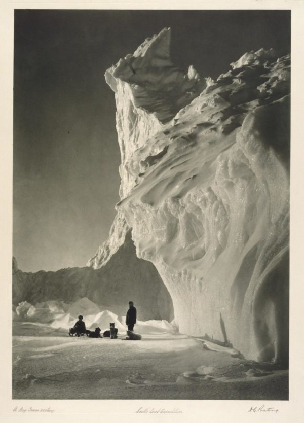  A black and white image of a cavern in an iceberg and some members of the expedition.